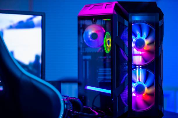 Un ordinateur de jeu de bureau doté d'un éclairage RVB et de ventilateurs de refroidissement visibles est placé à côté d'un moniteur dans une pièce à l'éclairage ambiant bleu.