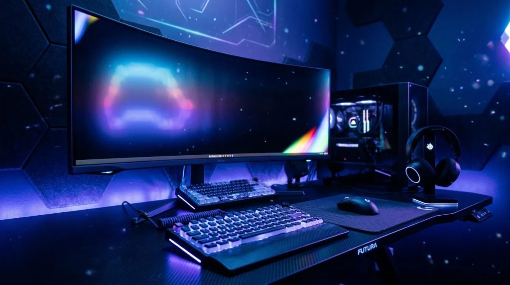 Une configuration de jeu moderne avec un moniteur incurvé ultra-large, un clavier mécanique, une souris, un casque et un PC de bureau avec éclairage RVB, le tout sur un bureau noir dans une pièce sombre et éclairée en bleu.